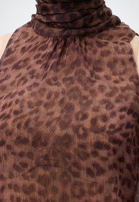 Haut marron sans manches avec motif léopard foncé et encolure haute froncée, montré du buste au cou.
