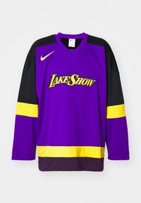 Purpura T-krekls no Nike ar garām melnām piedurknēm. Iezīmē "LAKE SHOW" dzeltenā krāsā, dzeltena akcenta josla un melna apakšmala.
