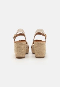 Beige plattform sandaler med flettede jute hæler, justerbar ankelrem og kryssdesign. Glatt læraktig materiale, brune accenter.