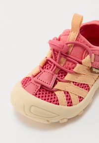 Baskets en maille rose avec semelle en caoutchouc crème, dotées de sangles jaunes et d'un design ajusté. Comprend un système de laçage à bascule pour un ajustement facile.