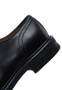 Zwarte leren schoen met een gladde textuur, gestikte accenten en een lage, textuur rubberen zool. Heeft een ronde neus en een instapontwerp.