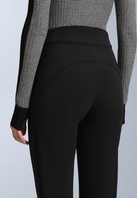 Fekete, magas derekú leggings sima textúrával. A derékpánt széles, és az anyag elasztikus, biztosítva a szoros illeszkedést.