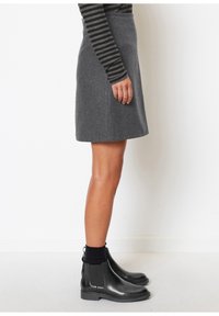 Jupe en laine grise à coupe droite, portée avec un haut à manches longues noir et gris à rayures et des bottines noires. Texture lisse.