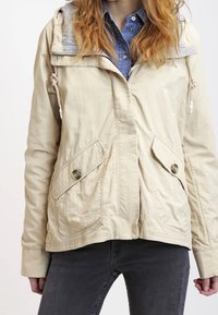 Beige letvægtsjakke med grå hætte, snore, to forlommer med knapper og en afslappet pasform. Tekstureret stof.