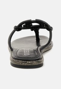 Tongs noires avec une semelle en cuir lisse, embellies par des accents argentés sur les côtés, et un support central pour l'orteil. Nom de la marque visible sur le semelle intérieure.