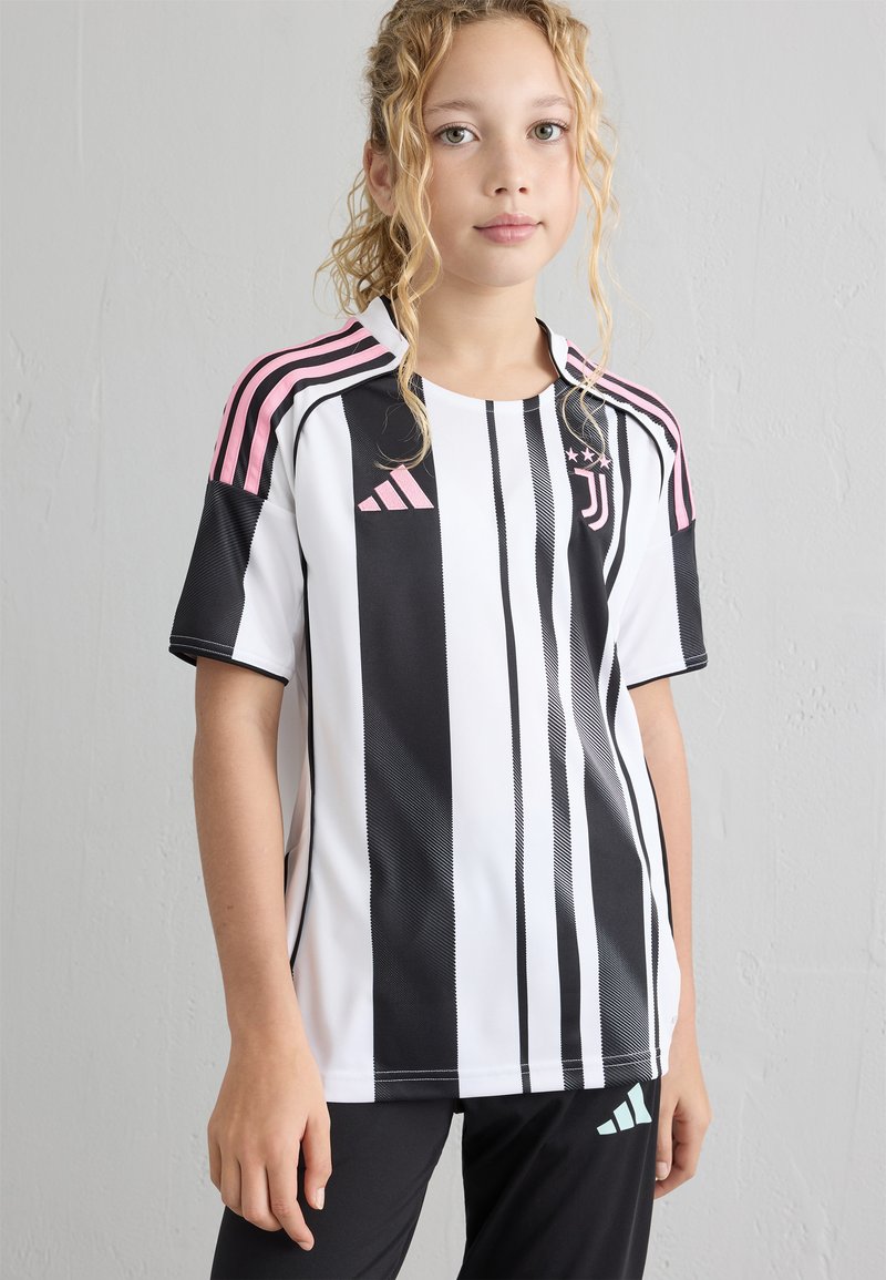 Jersey de rayas blancas y negras con acentos rosas en los hombros y logo de Adidas. Mangas cortas, material sintético con una textura suave.
