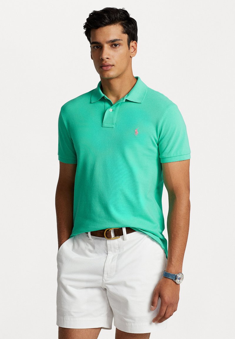 Polo en vert menthe vif, en tissu coton, à manches courtes, avec une patte de boutonnage à trois boutons et un petit logo brodé sur la poitrine.