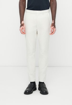 Vita slim-fit byxor med en slät textur, sidfickor och knappstängning, kombinerat med svarta läder loafers.