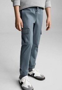 Světle modré cargo kalhoty se dvěma bočními kapsami, elastickými manžetami a páskem na stažení, doplněné bílými teniskami se šedými akcenty.