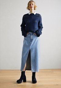 Pull en maille bleu marine avec un large col associé à une jupe en denim bleu clair avec une fente sur le devant, complétée par des bottes à talons noires.