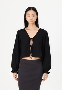 Blusa nera corta con scollatura a V profonda, maniche lunghe a palloncino e chiusura con lacci sul davanti. Realizzata in tessuto leggero con una consistenza morbida.