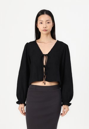 Zwarte cropped blouse met een diepe V-hals, lange ballonmouwen en een striksluiting aan de voorkant. Gemaakt van een lichtgewicht stof met een zachte textuur.