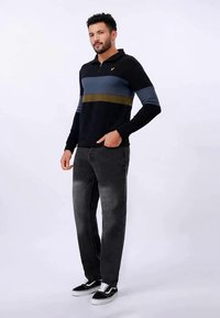 Pullover de manga longa preto com riscas horizontais em cinza e verde-azeitona; combinado com jeans cinza e ténis pretos.
