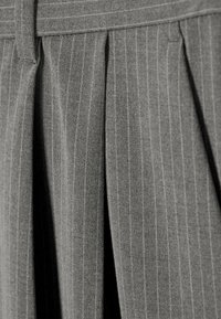 Tissu gris avec de fines rayures blanches verticales et de larges plis, doté d'une taille avec passants de ceinture.