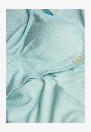 Hellblauer Rippstoff-Bralette mit weicher Textur, ausgestattet mit einem goldenen Logo-Akzent und verstellbaren Trägern, drapiert auf einer flachen Oberfläche.