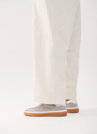 Grå semskede sneakers med hvite detaljer og en gummisåle, med et teksturert design og flate snørebånd, parret med lyse beige bukser.