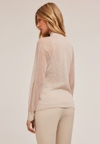 Helles beige Pullover mit gerippten Akzenten an den Ärmeln, weichem Strickstoff, Stehkragen-Design und glattem Finish auf der Rückseite.