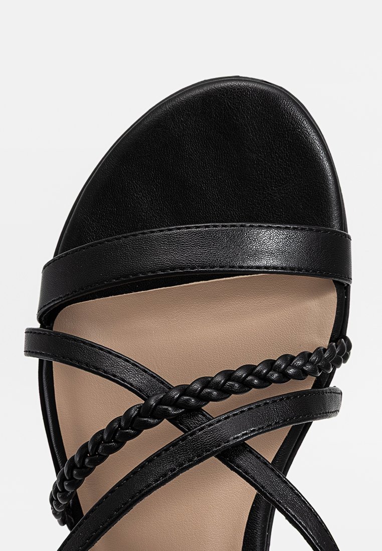 Sandale noire avec des brides tressées, une texture en cuir lisse, un design à bout ouvert et une semelle de couleur neutre.