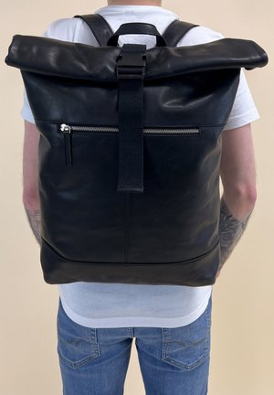 Black leather roll-top backpack with a zipper pocket, adjustable straps, and a textured finish. Features subtle branding at the bottom.
