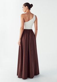 Een wit geribbeld topje met één schouder, gecombineerd met een lange, donkerbruine rok met elastische taille. Gladde textuur en vloeiende pasvorm.