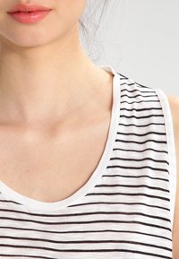 Canottiera bianca con sottili righe nere, caratterizzata da un scollo arrotondato e design senza maniche. La texture morbida è evidente nel tessuto.