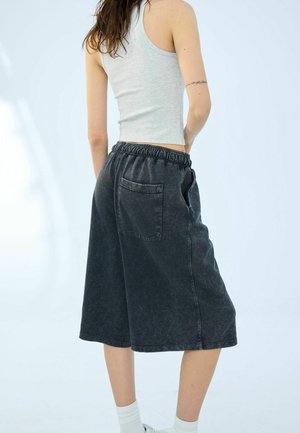 Person wearing a sleeveless gray top and loose black knee-length shorts with an elastic waistband, standing against a light background.