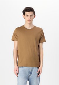 Brun bomull T-skjorte med korte ermer, rund hals og en liten logo på brystet. Kombinert med lyseblå denim jeans.