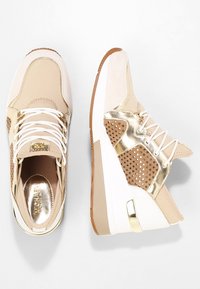 Sneakers beige con dettagli metallici dorati, design perforato, lacci bianchi, suola spessa in gomma e logo dorato sulla soletta.