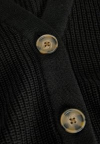 Mustvalge kudumiga kardigan V-kaelusega, millel on kaks ümmargust marmorist nuppu. Tekstuur on pehme ja ribakujuline.