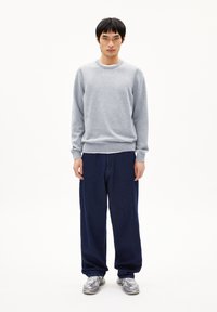 Grauer Sweatshirt aus weichem Stoff mit Rundhalsausschnitt, ergänzt durch locker sitzende marineblaue Hose und silberne Sneaker. Minimales Design.