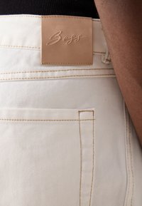 Lysfargede denimjeans med teksturert overflate, utstyrt med en lærmerkelapp og kontrastfargede sømmer på baklommen.