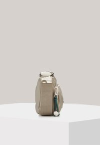 Beige bag with a soft, structured form. Features a zippered side pocket, a sturdy strap, and a decorative green accent. Smooth texture.