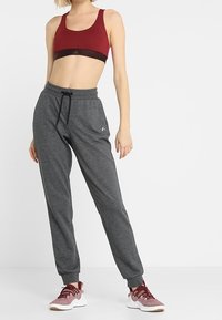 Top corto atlético rojo con banda negra, pantalones jogger grises con puños elásticos y zapatillas color burdeos y blancas, que muestran un atuendo deportivo.