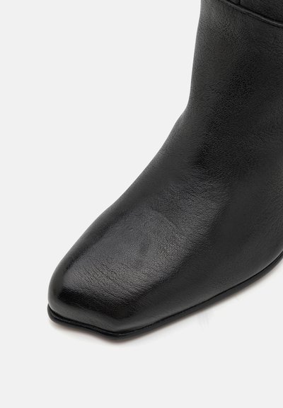 Sort læder ankelstøvle med en glat overflade, firkantet tå og minimale syninger. Slank design med en let forlænget form.