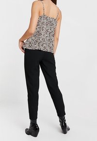 Svarta slim-fit byxor i kombination med en krämfärgad topp med svarta prickar. Toppens har tunna axelband och en lös, luftig passform. Glansiga svarta klackboots.