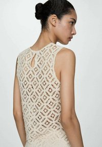 Lace top in cream with a geometric pattern, featuring a keyhole opening at the back and a textured finish.