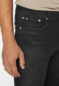 Svarta jeans i denim med slim fit, prydda med silverdetaljer, framfickor och en liten svartvit CK-logotyp på midjebandet.