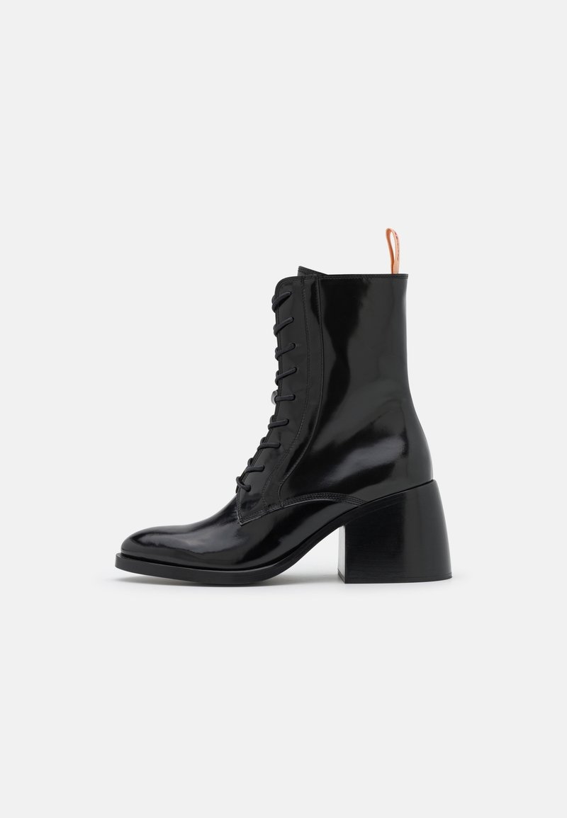 Bottines en cuir verni noir avec un bout rond, un laçage à l'avant et un talon bloc épais et haut ; présentant une languette à boucle contrastante.