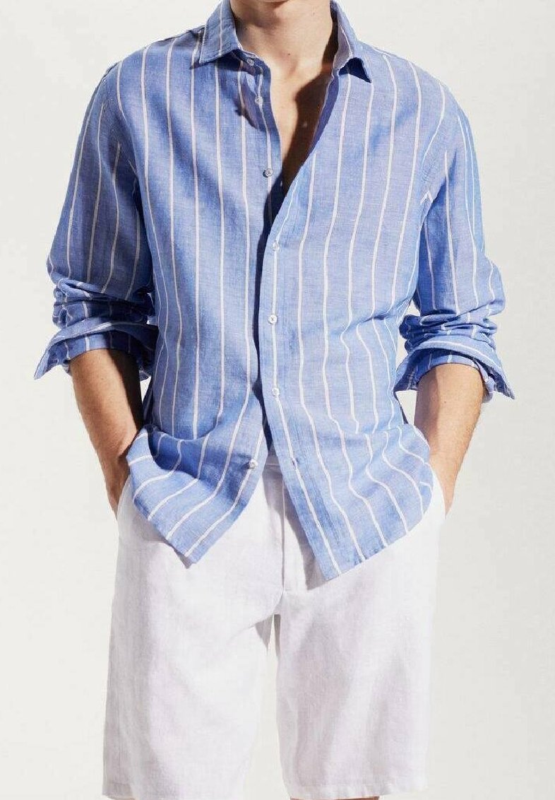 Chemise en lin rayée bleue et blanche avec un devant à boutons, des manches retroussées et une coupe décontractée, associée à un short blanc.