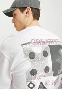 Camiseta blanca de algodón con un gran diseño gráfico en negro y gris, con "CREATIVE" en rosa, y una gorra texturizada.