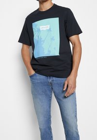 Černé bavlněné tričko se světle modrým motivem, na kterém jsou palmy a uprostřed logo "Levi's", doplněné modrými džínami z denimu.