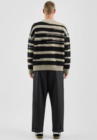 Sweter dzianinowy z poziomymi czarno-beżowymi paskami, z okrągłym dekoltem i luźnym krojem. Połączony z luźnymi czarnymi spodniami i wzorzystymi butami.