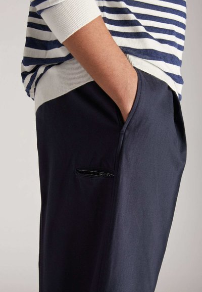 Dunkelblaue Hosen mit einer Seitentasche und einem schwarzen Reißverschluss. Kombiniert mit einem weiß-blauen gestreiften Oberteil, das die Stoffstruktur zeigt.