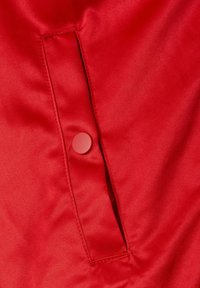 Rødt satinstof med en knappet lomme med klap, der viser en glat tekstur og en lys, blank finish.
