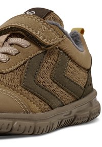 Bruna sneakers med en texturerad canvasovandel, som har ett kardborreband och snörning, samt gummisula med zigzagdetaljer.