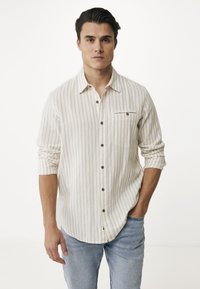 Crème en beige gestreepte overhemd met lange mouwen, een button-down kraag, een borstzak en bruine knopen; gedragen met lichtblauwe spijkerbroek.