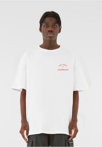 White cotton t-shirt with a loose fit, rounded neckline, and short sleeves. Features red printed text "FREE SPIRIT 2021 MJGONZALES."