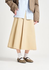 Falda midi A-line beige, camisa de botones azul clara, chaqueta bomber marrón, combinada con bailarinas de leopardo y calcetines blancos con volantes.