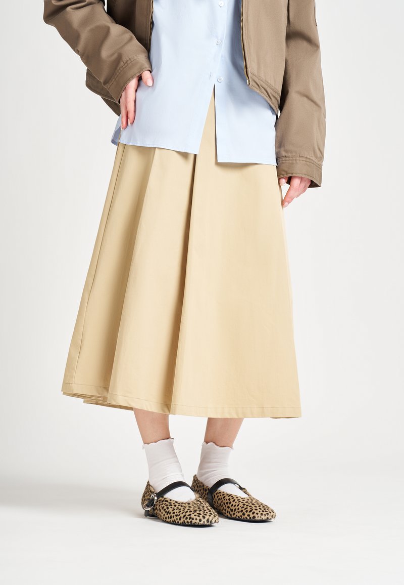 Falda midi A-line beige, camisa de botones azul clara, chaqueta bomber marrón, combinada con bailarinas de leopardo y calcetines blancos con volantes.