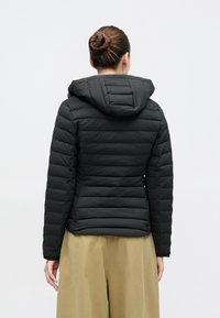 Fekete kapucnis steppelt puffer dzseki, karcsúsított fazonnal. Simább textúra és rugalmas mandzsetták. Világos barna nadrággal párosítva.